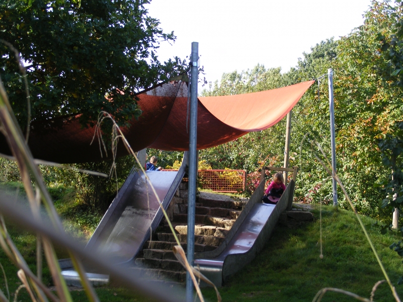 Der Rutschberg auf unserem Spielplatz hat 2 unterschiedlich breite Rutschen. Sie sind über den Grashang, die Natursteintreppe oder den befestigten Weg zu erreichen. ein Sonnensegel spendet Sc