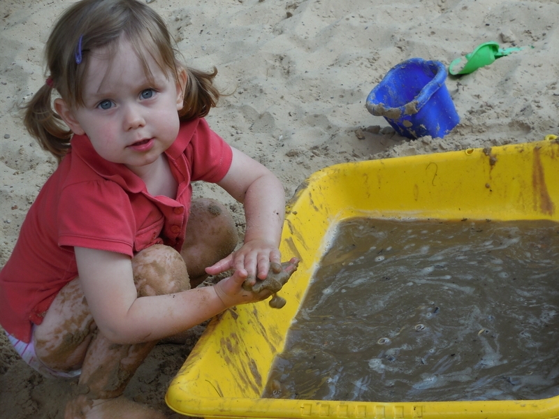 Kind beim Matschen mit Sand und Wasser.